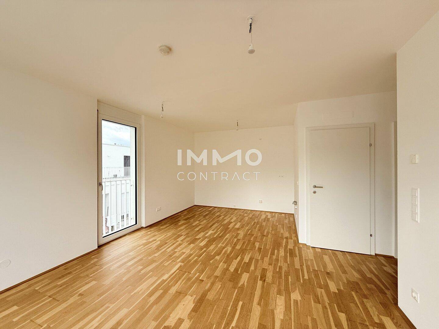 Leeres Zimmer mit hellem Parkettboden und Zugang zu einem Außenbereich durch eine Glastür.