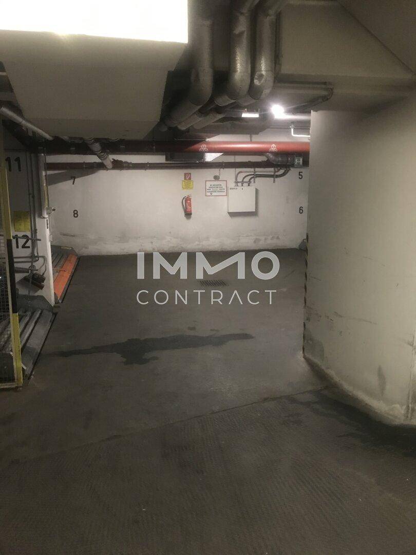 Innenansicht einer Tiefgarage mit nummerierten Stellplätzen, Feuerlöscher und sichtbaren Rohren.