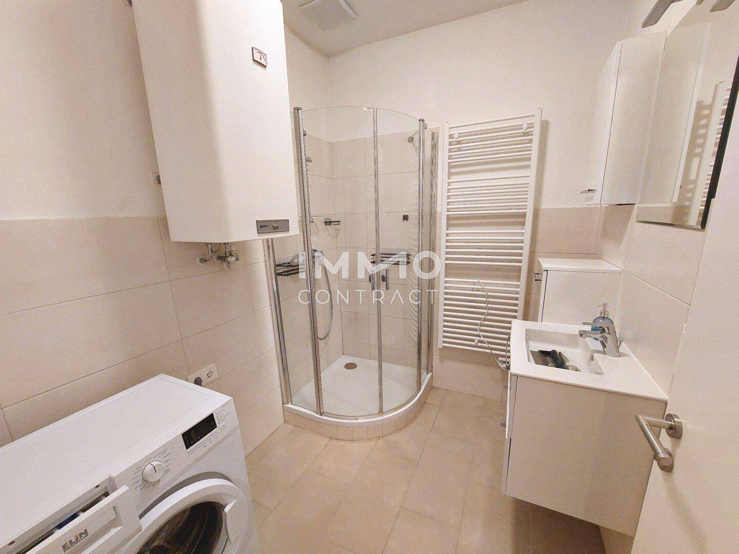 Helles Badezimmer mit Duschkabine, Waschbecken, WC, beheiztem Handtuchhalter und Waschmaschine.