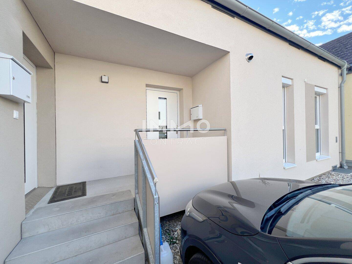 Moderne Hausfassade mit Eingangsbereich und einem geparkten Auto davor.