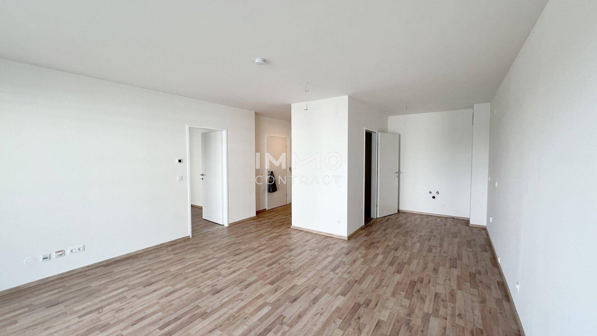 Helles Wohnzimmer mit Laminatboden und Zugang zu weiteren Räumen, in neuwertigem Zustand.