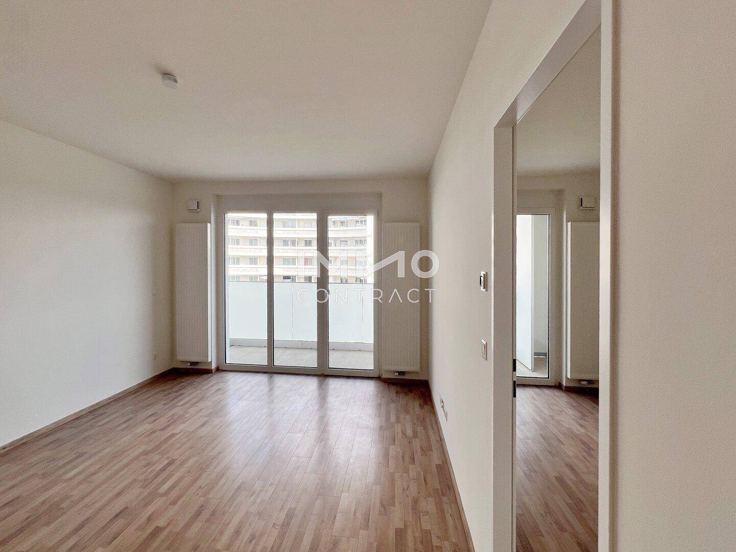 Geräumiges Wohnzimmer mit Laminatboden und großen Fenstern, die Zugang zum Balkon bieten.