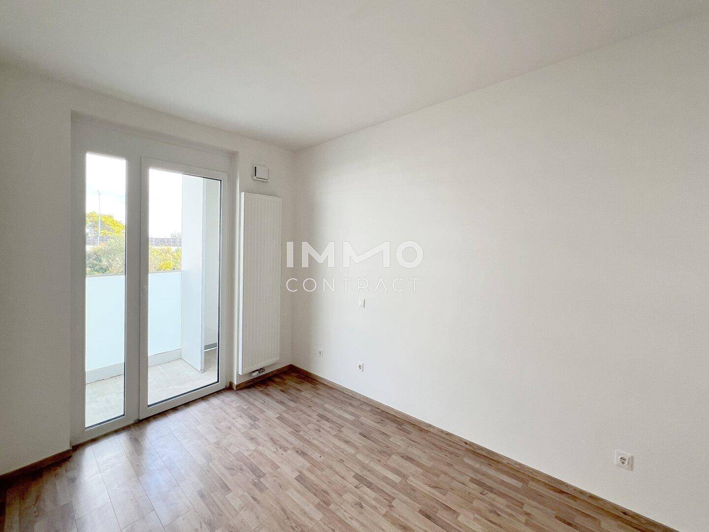 Schlafzimmer mit Laminatboden und Balkonzugang, das viel natürliches Licht erhält.
