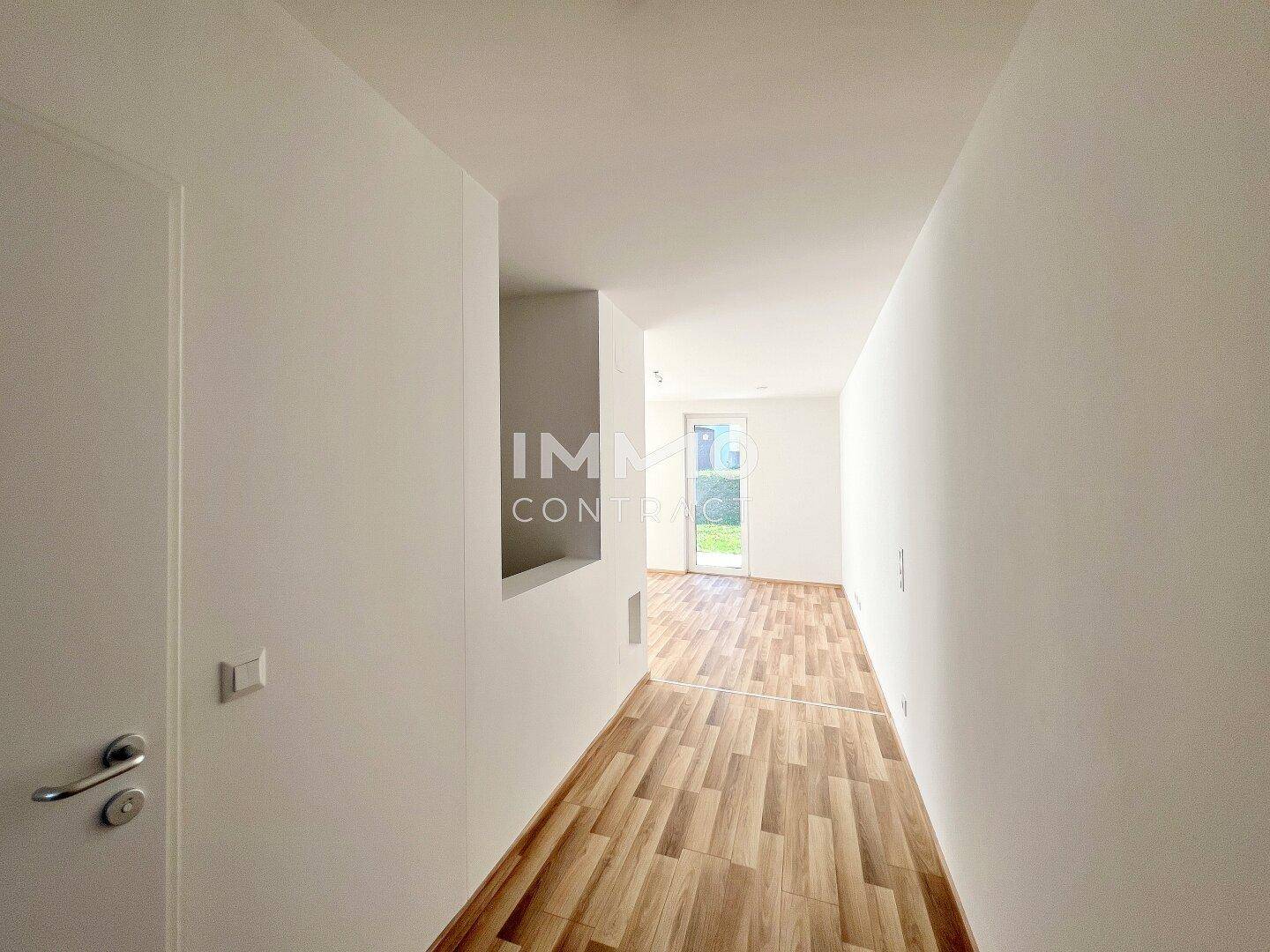 Moderner Flur mit Holzboden und weiß gestrichenen Wänden, der zu weiteren Räumen führt.
