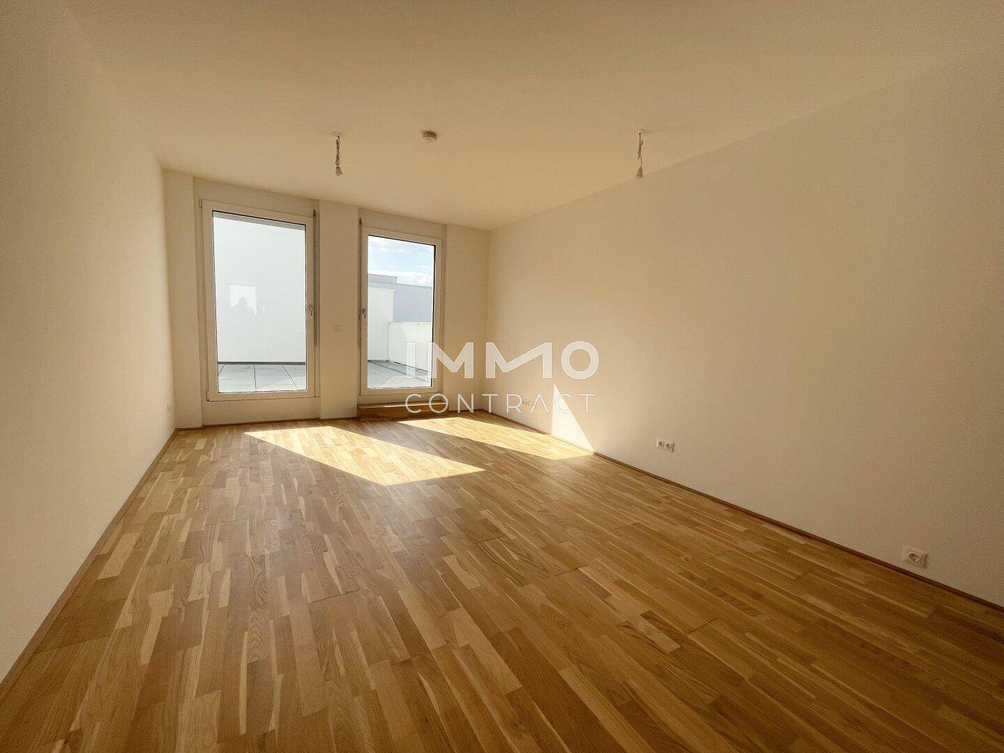 Helles, leeres Zimmer mit Holzboden und großen Fenstertüren zur Terrasse.