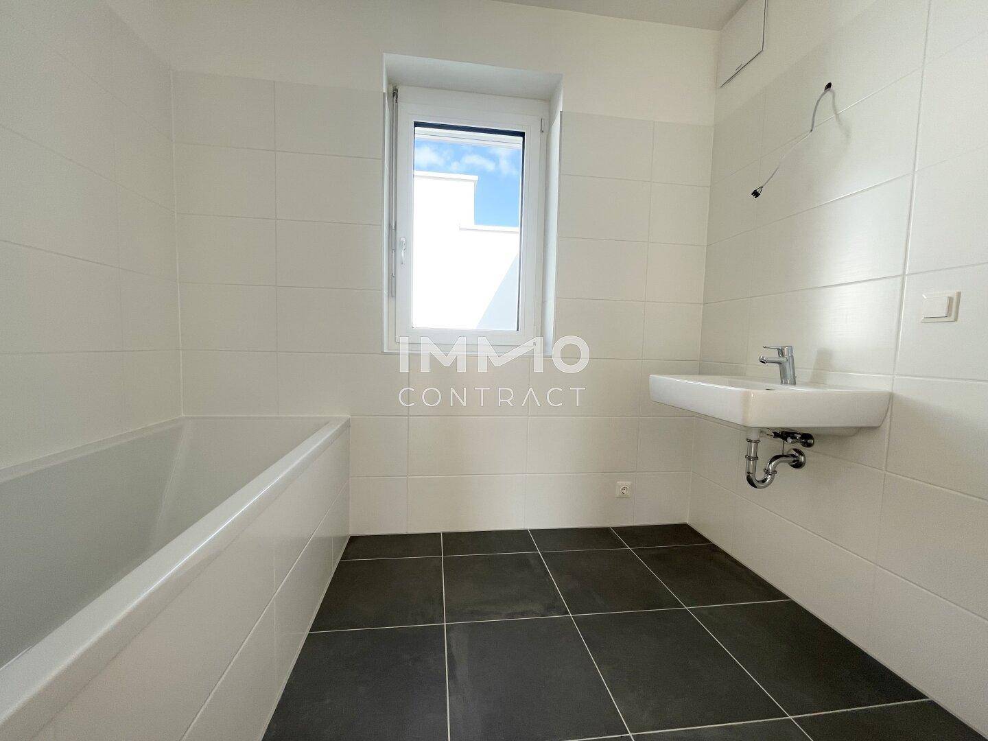 Modernes Badezimmer mit Badewanne, Einzelwaschbecken und Fenster für Tageslicht.