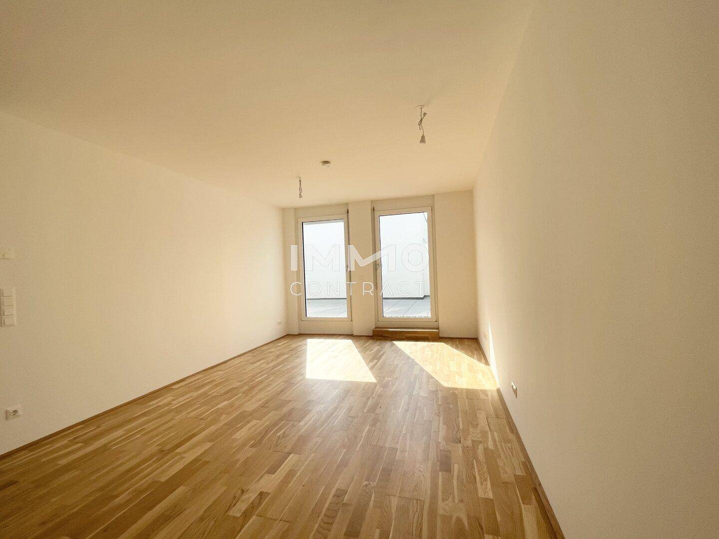 Lichtdurchfluteter Raum mit warmem Holzboden und direktem Zugang zur Außenterrasse.