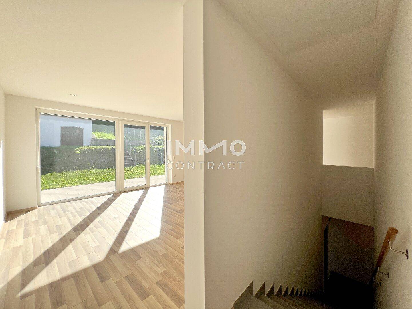 Eingangsbereich mit Treppe und Zugang zu einem hellen Wohnraum mit großen Fenstern.