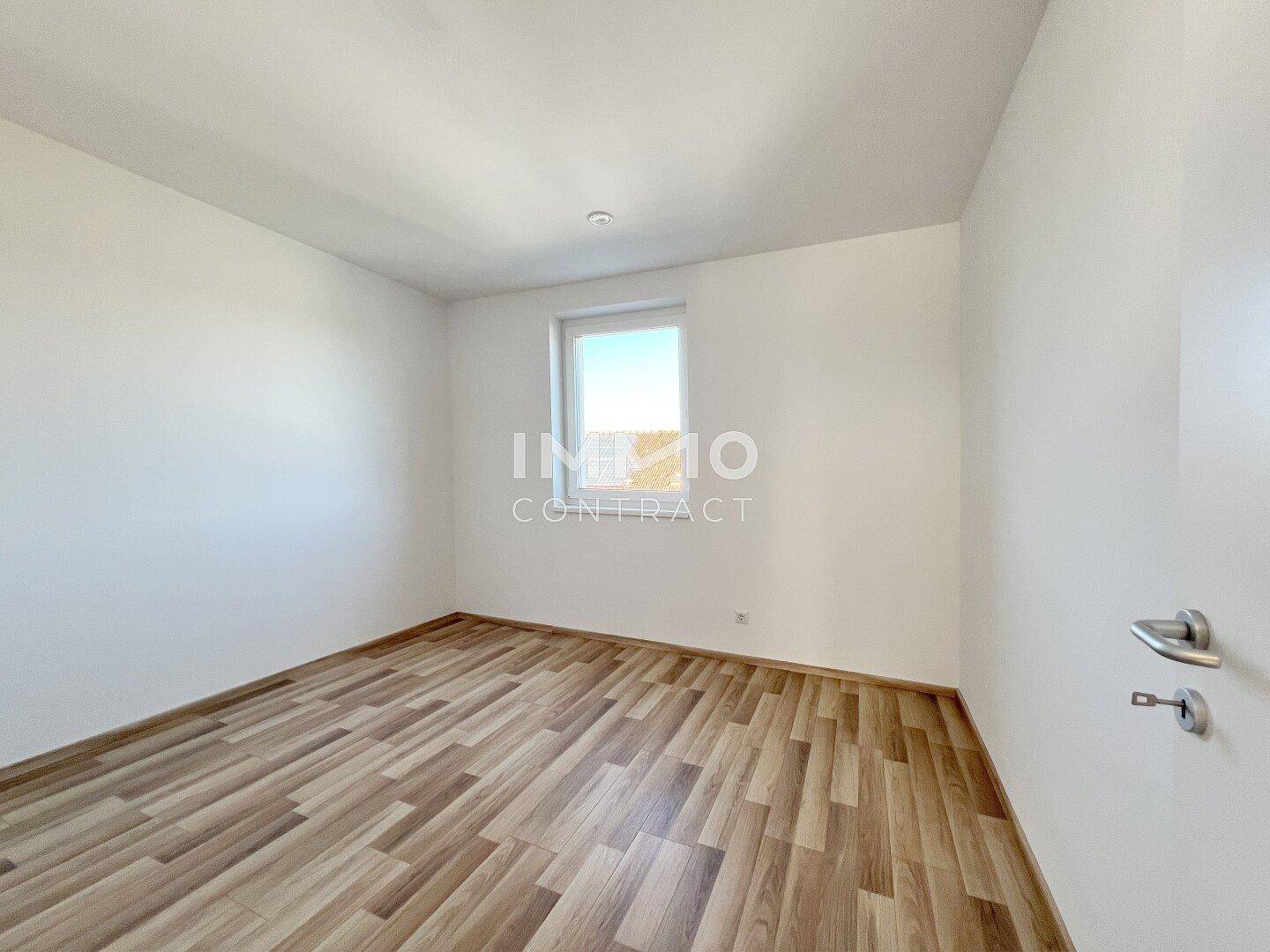 Helles Schlafzimmer mit Holzboden und einem Fenster, bereit zur individuellen Gestaltung.