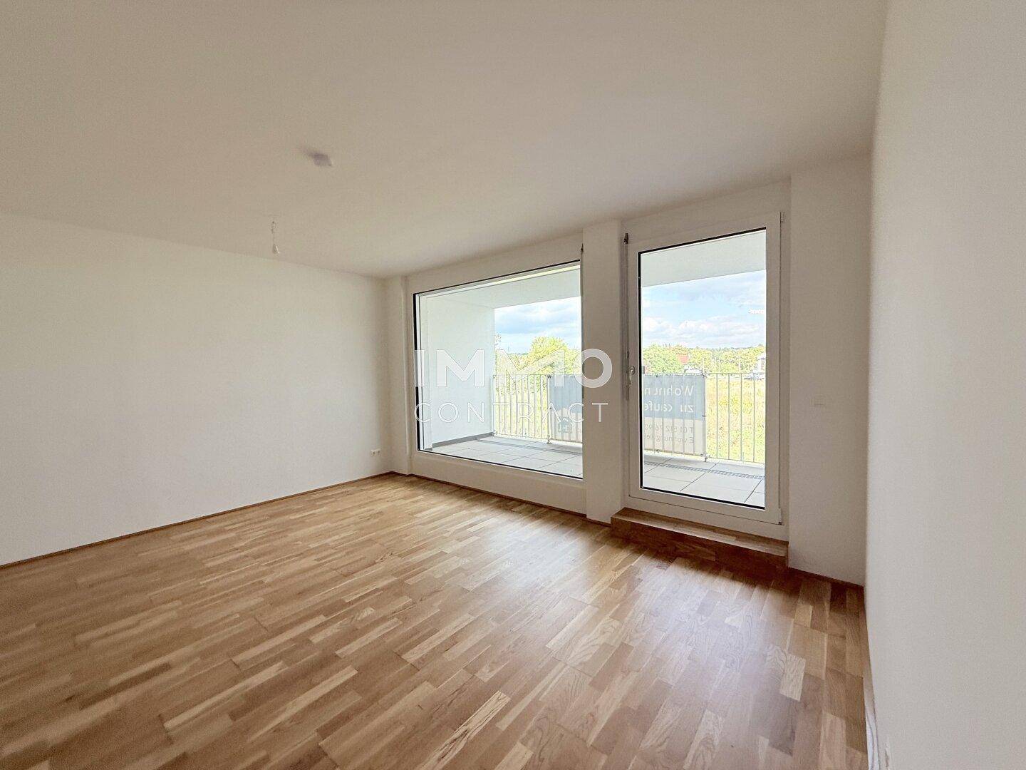 Lichtdurchflutetes Wohnzimmer mit Parkettboden und Zugang zu einem Balkon.