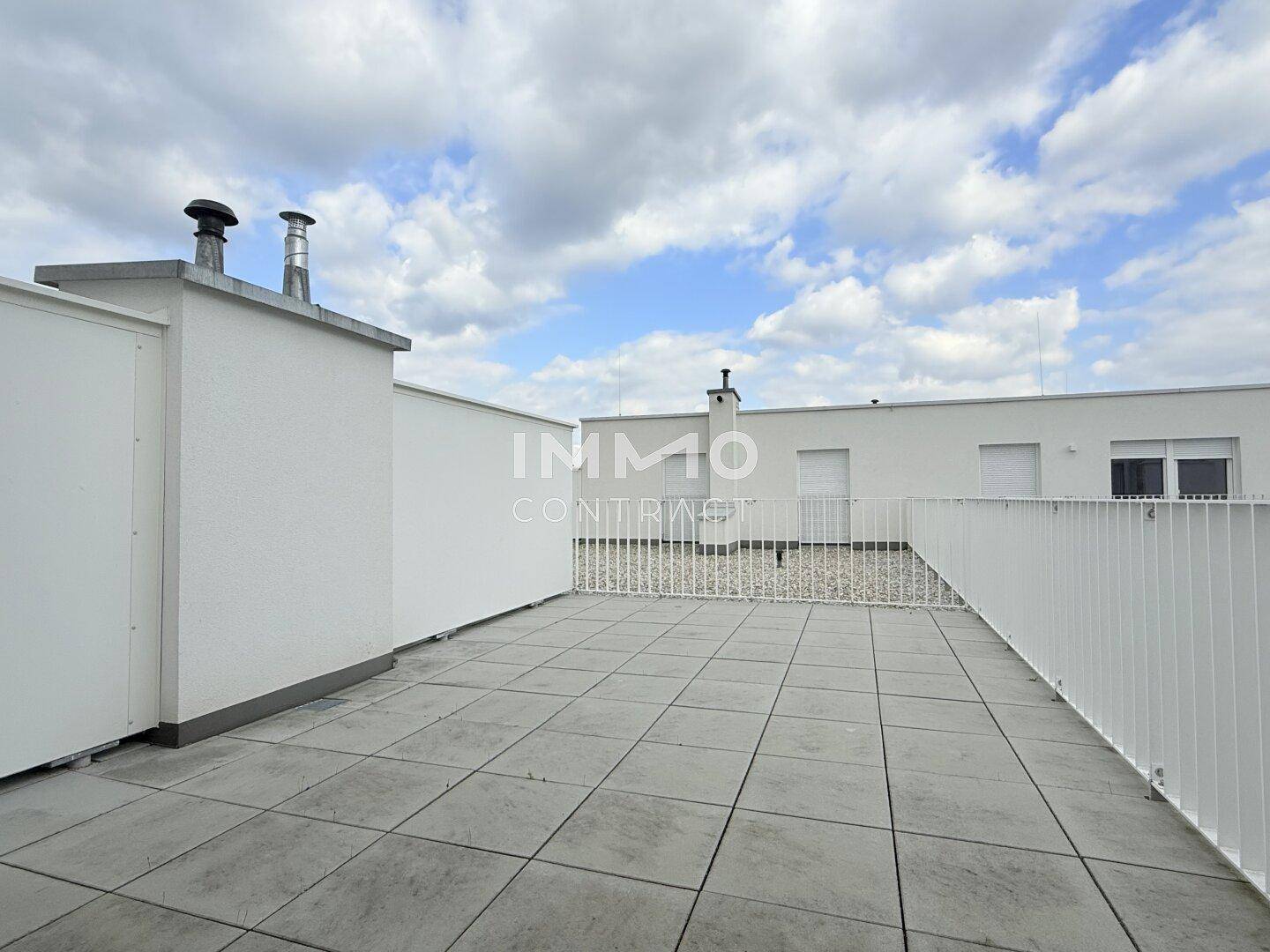Geräumige Dachterrasse mit Fliesenboden und weißem Geländer unter bewölktem Himmel.