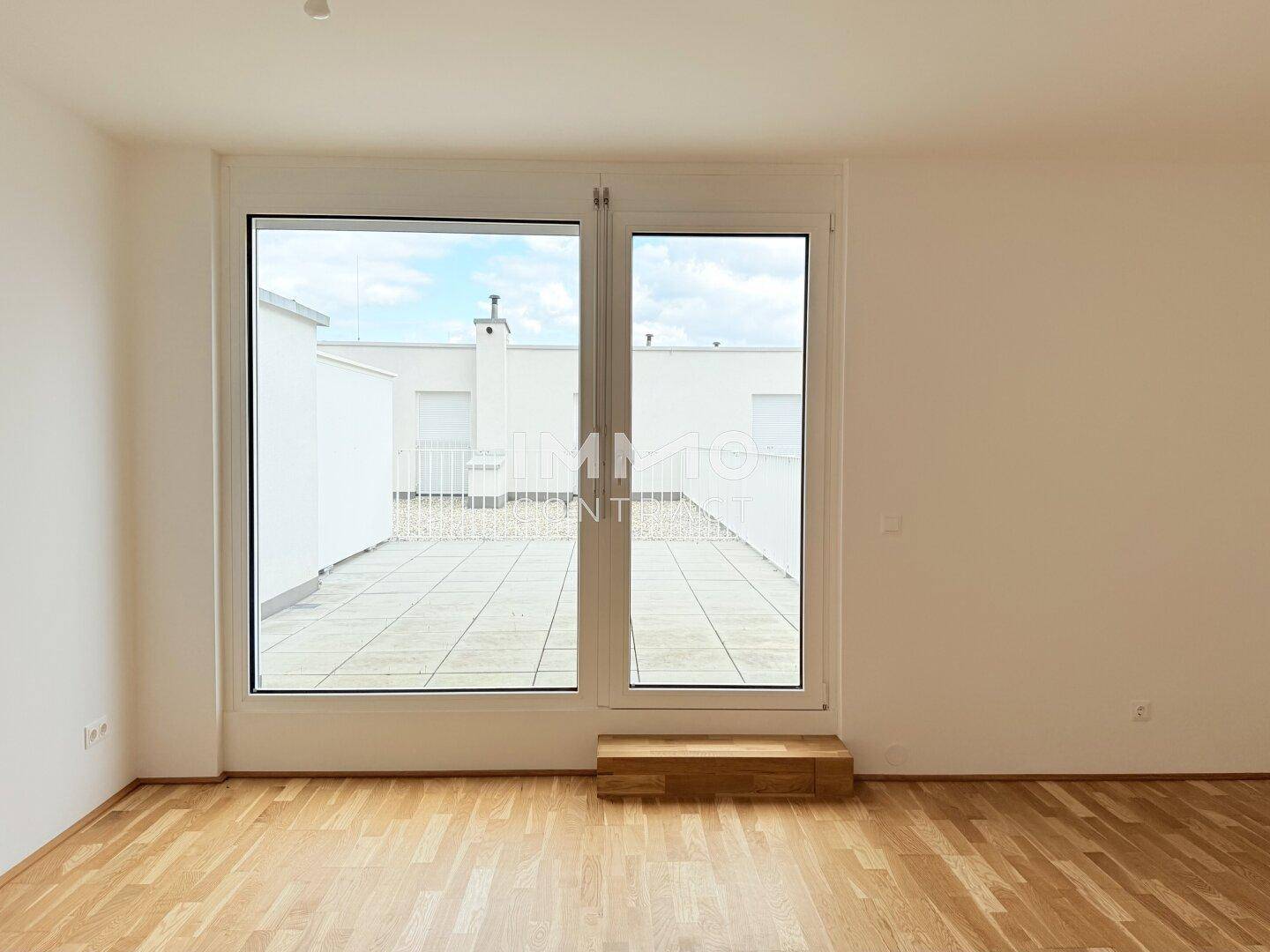 Heller Raum mit Parkettboden und großen Fenstern, die den Blick auf die Dachterrasse freigeben.