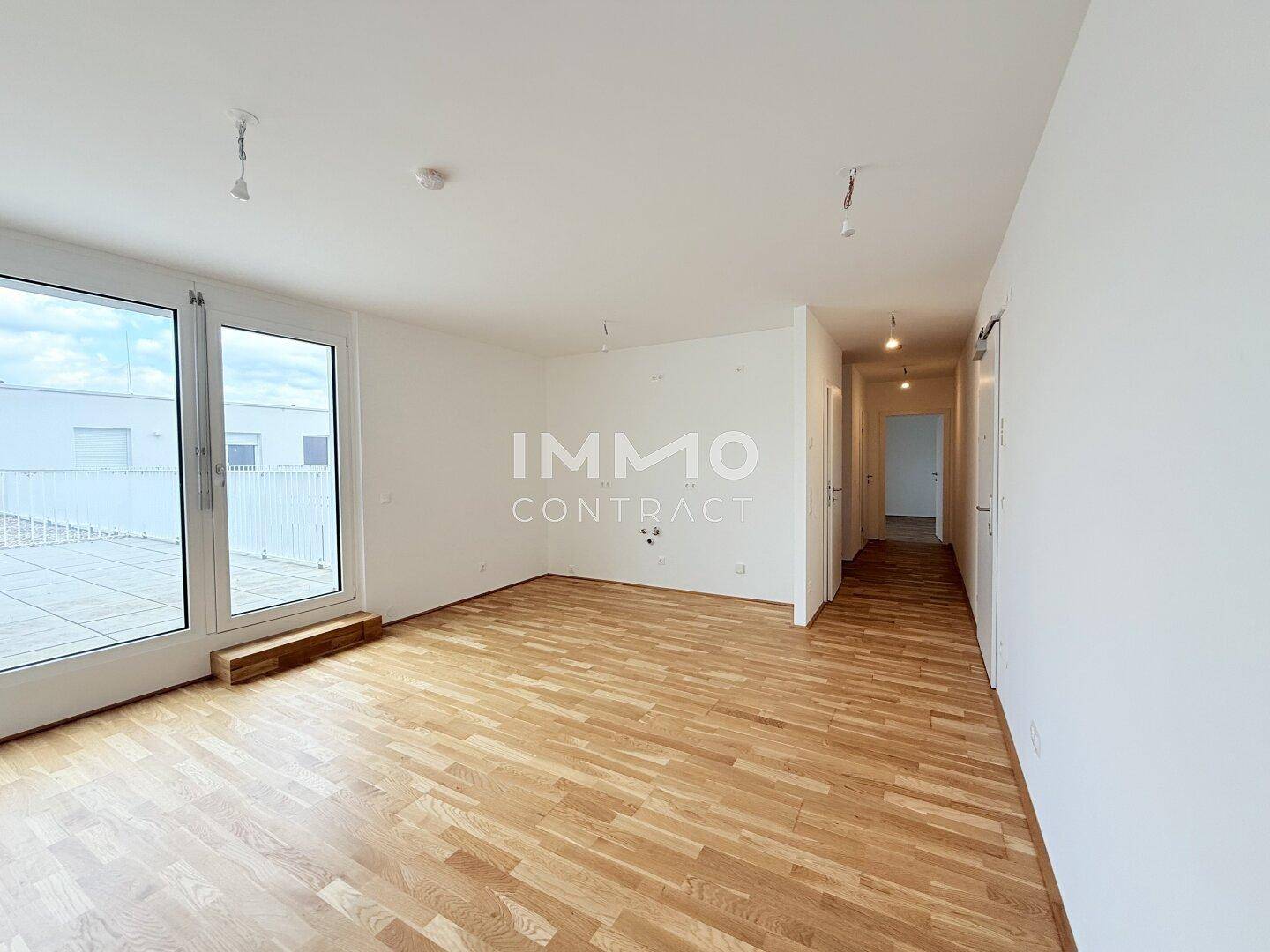 Geräumiges, leeres Wohnzimmer mit Parkettboden und Zugang zu einer großen Terrasse.