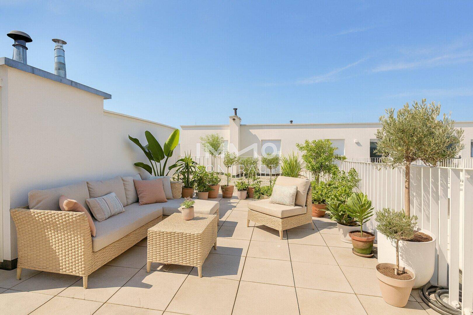 Möblierte Dachterrasse mit Pflanzen, Sitzgelegenheiten und hellem Fliesenboden unter blauem Himmel.
