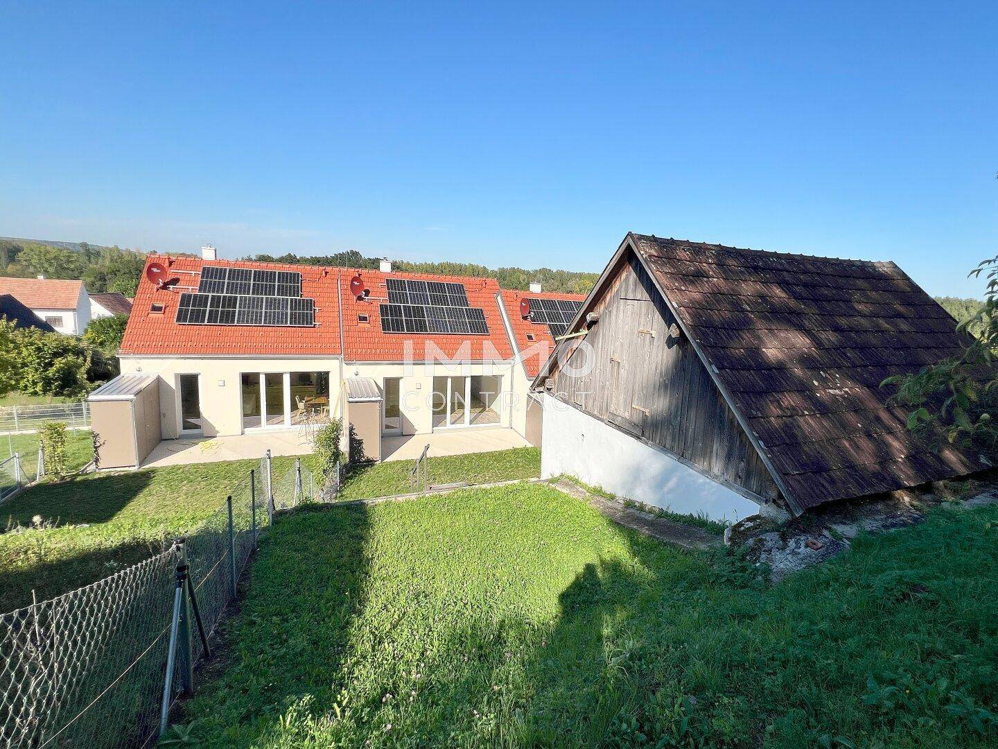 Panoramablick auf die neuen Häuser mit Solaranlagen und das alte Nebengebäude in der grünen Landschaft.