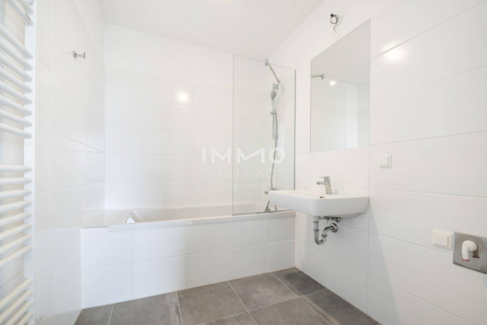 Modernes Badezimmer mit weißen Fliesen, Badewanne mit Duschabtrennung und Waschbecken.