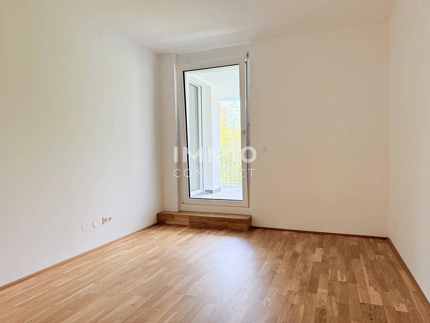 Helles Schlafzimmer mit Parkettboden und Zugang zu einem Balkon, ideal für frische Luft.