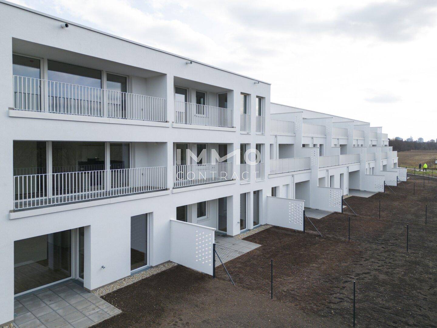 Moderne Wohnanlage mit Balkonen und Terrassen, umgeben von unbebautem Land.