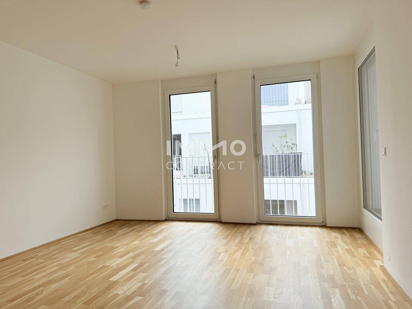 Lichtdurchflutetes Zimmer mit Holzboden und großen Fenstertüren zu einem Balkon.