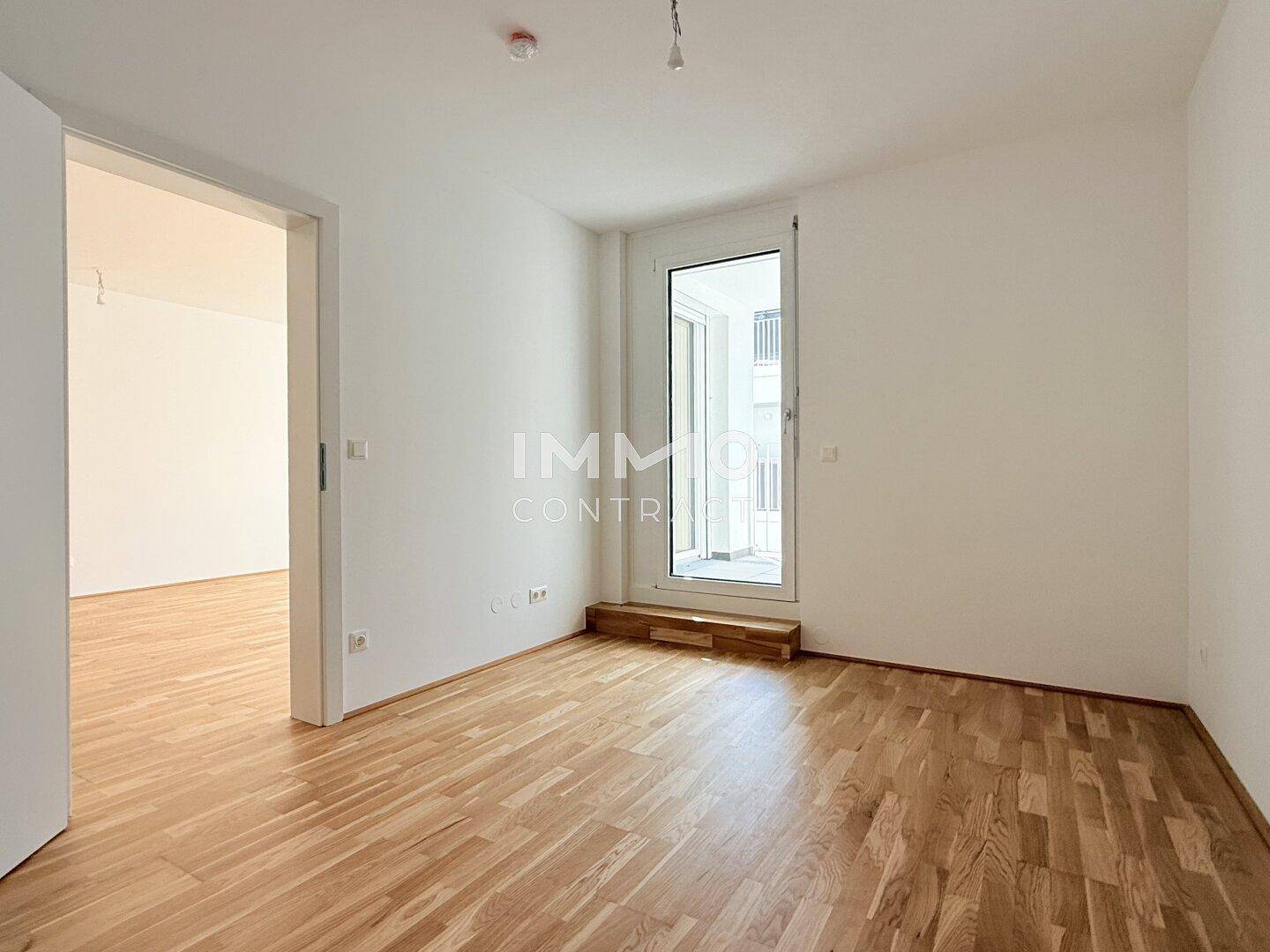 Leeres Zimmer mit Holzboden und Zugang zu einem Balkon, bereit zur individuellen Gestaltung.