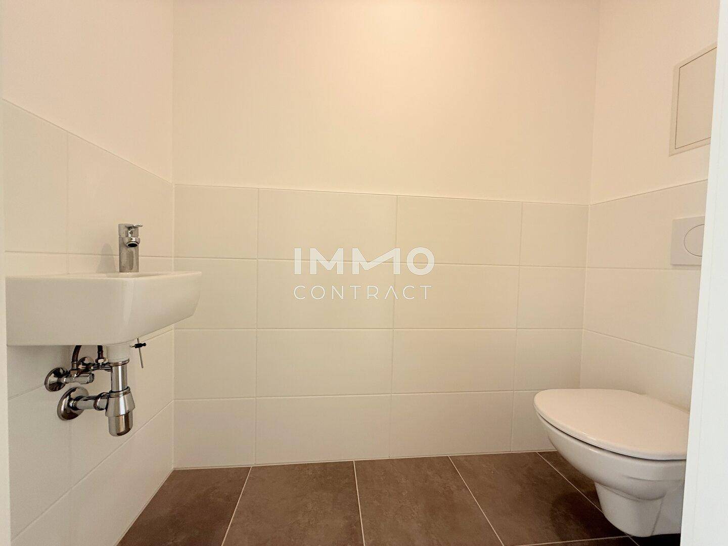 Funktionale Gästetoilette mit wandmontiertem WC, kleinem Waschbecken und Fliesenboden.