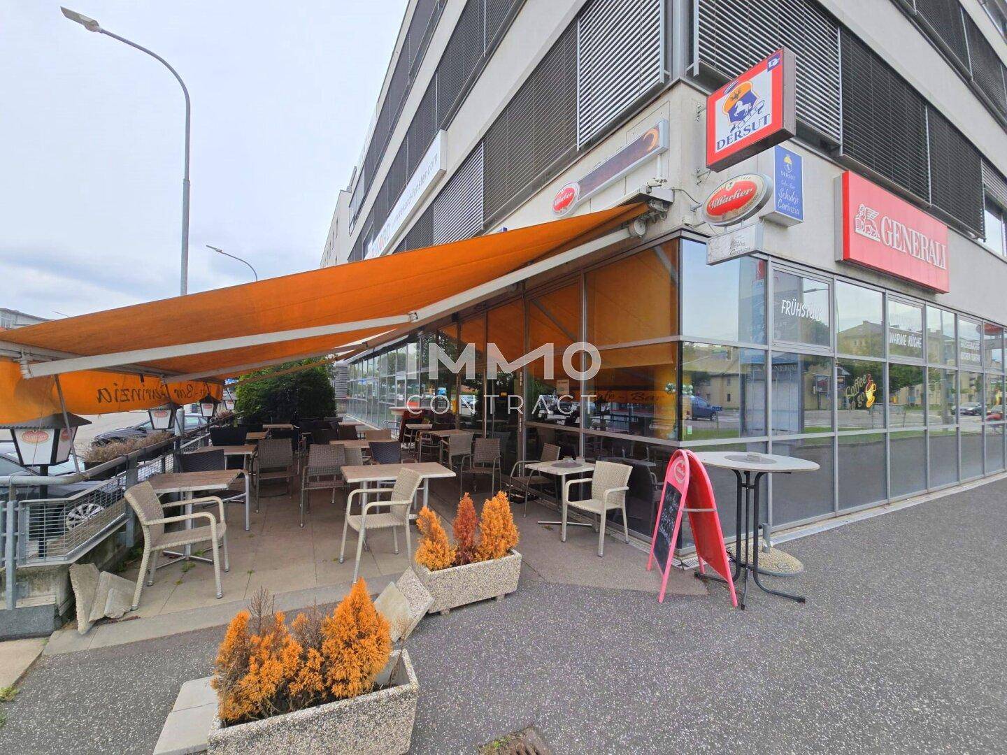 Außenterrasse des Cafés mit Tischen, Stühlen und einer großen orangefarbenen Markise.