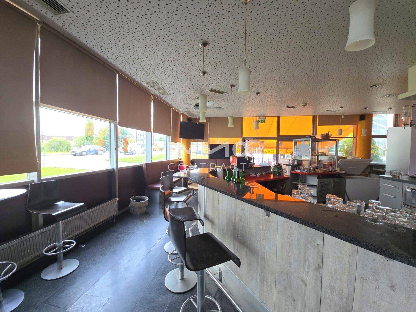 Gemütlicher Café-Sitzbereich mit Barhockern, großen Fenstern und Blick auf die Straße.