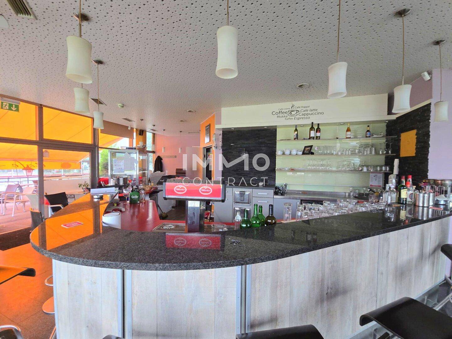 Innenansicht einer modernen Bar mit Granittheke, Hängelampen und Blick auf die Außenterrasse.