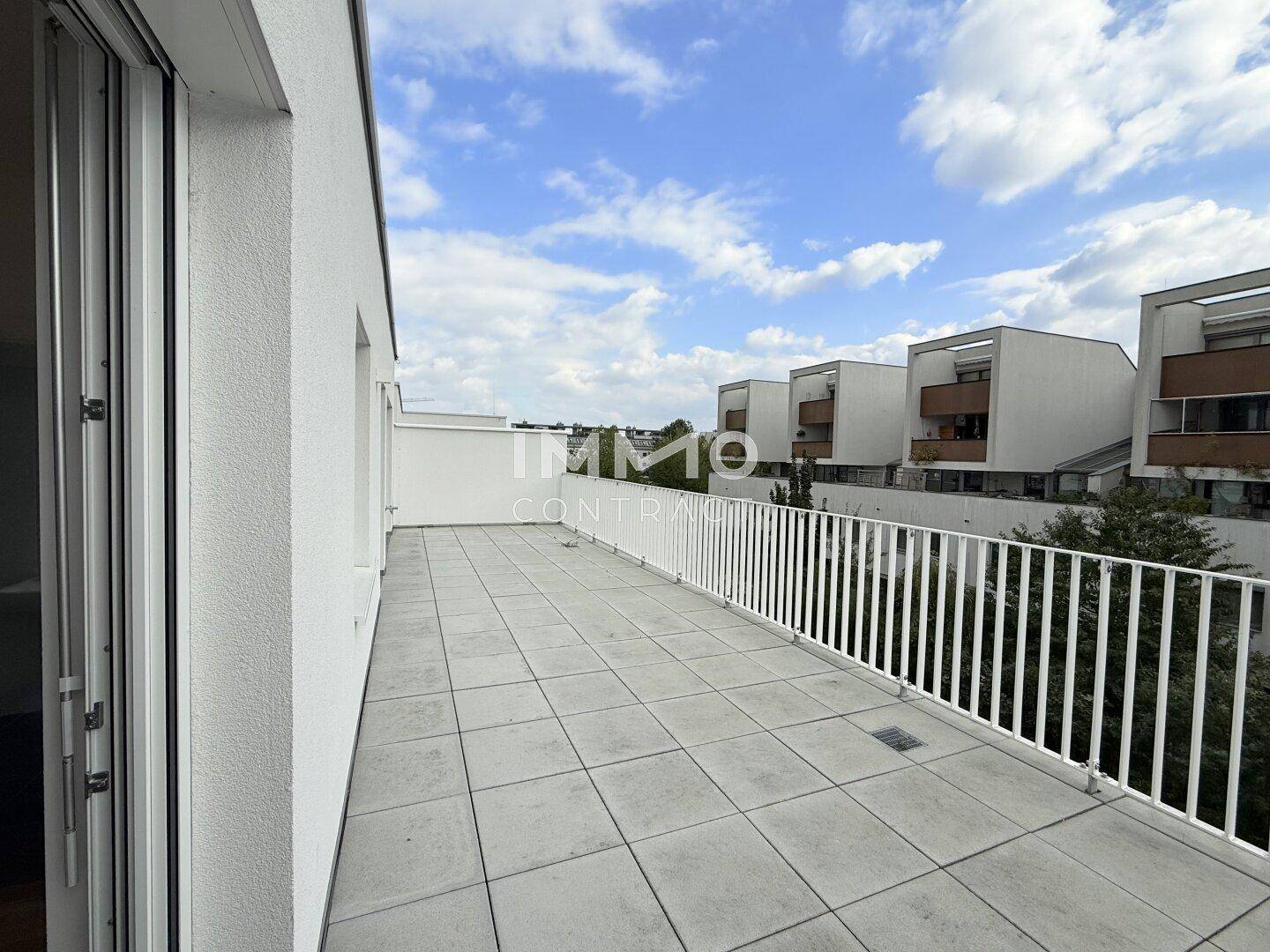Lange, geflieste Terrasse mit weißem Geländer und Blick auf die umliegenden Gebäude.
