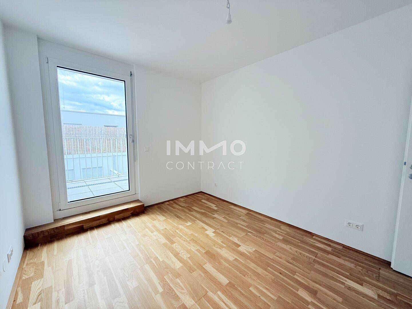 Helles Zimmer mit Parkettboden und großem Fenster, das viel Tageslicht hereinlässt.