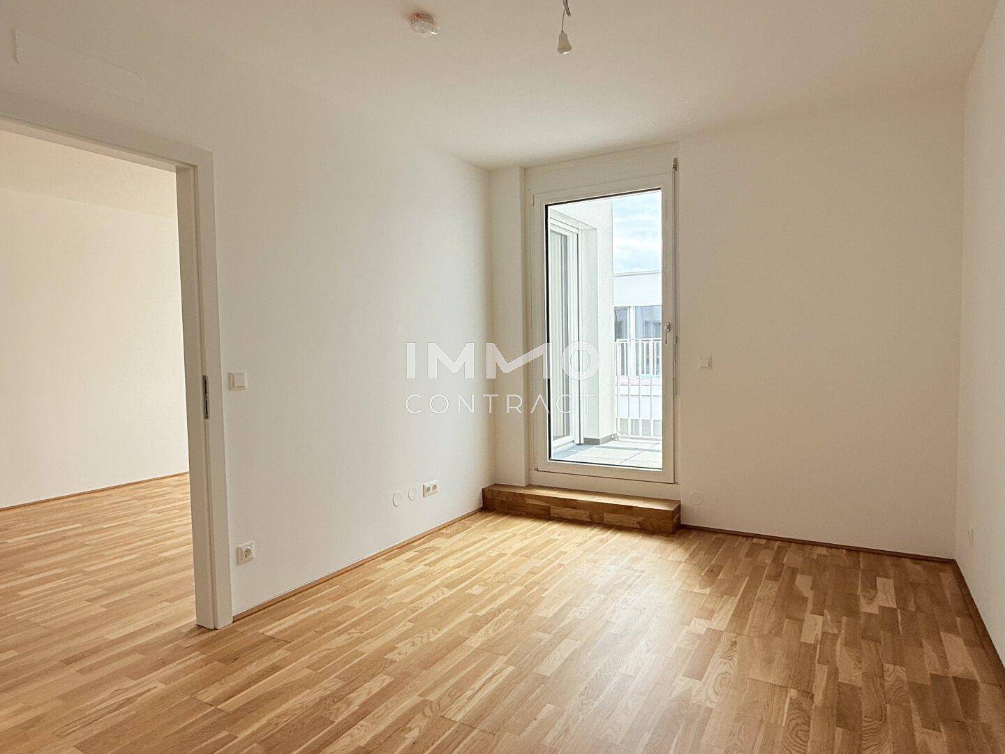 Leeres Zimmer mit Parkettboden und direktem Zugang zu einem kleinen Balkon.