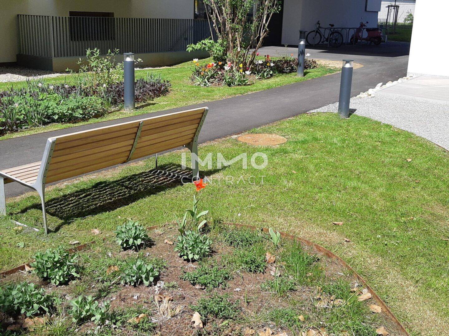Gepflegte Grünfläche mit Sitzbank, Blumenbeeten und Wegen im Außenbereich der Wohnanlage.