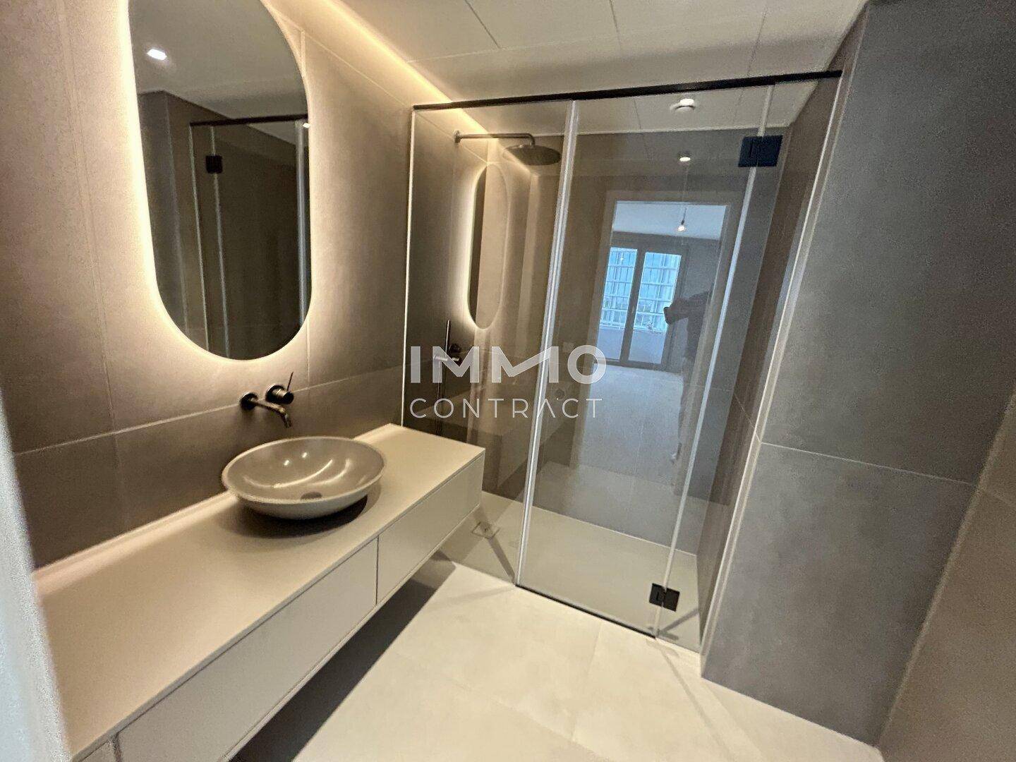 Elegantes Badezimmer mit begehbarer Dusche, modernem Waschbecken und beleuchtetem Spiegel.