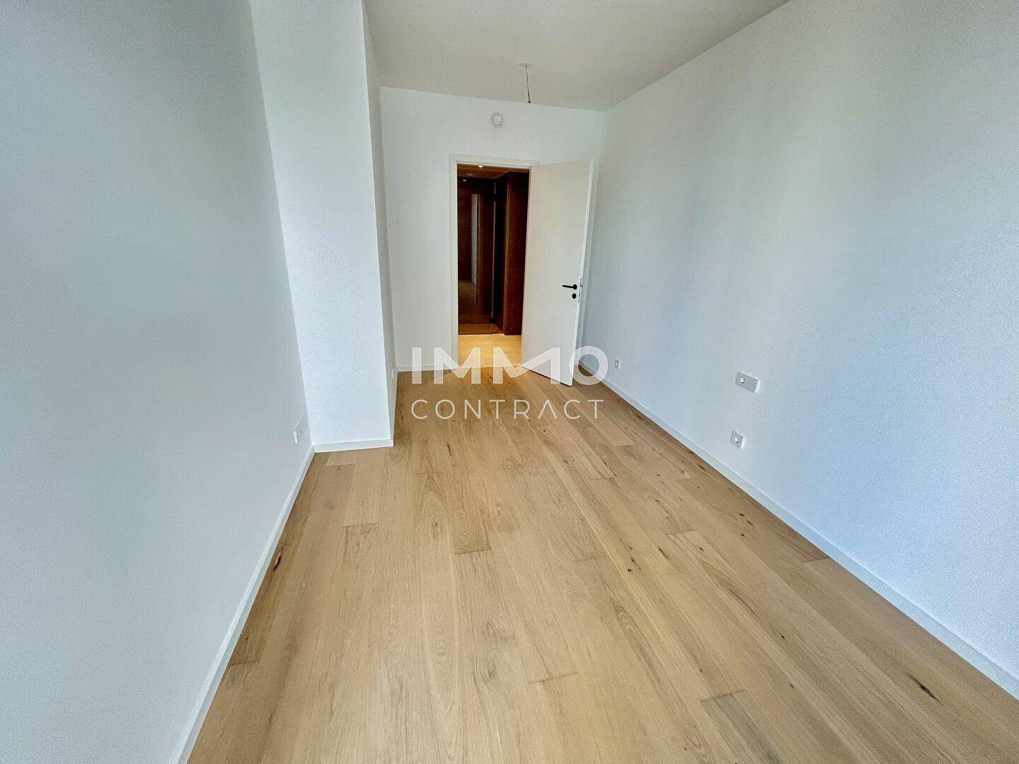 Heller Flur mit Holzparkettboden, weißen Wänden und Zugang zu weiteren Räumen.