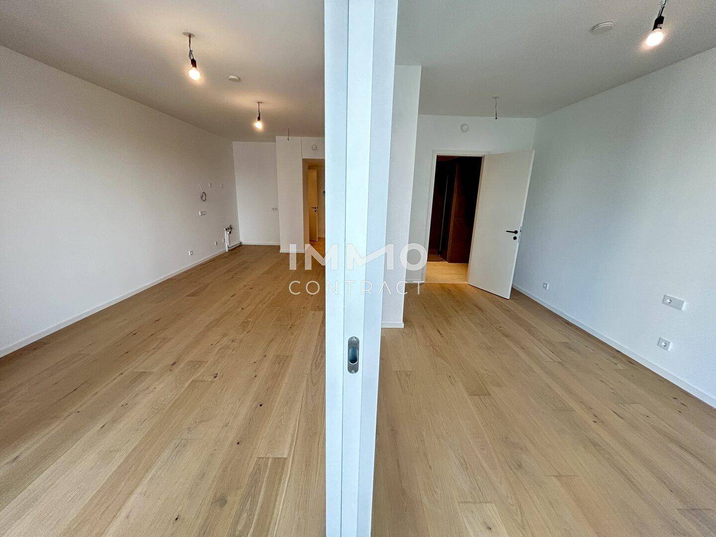 Geräumiger, unmöblierter Raum mit hellem Holzparkett und moderner Beleuchtung.