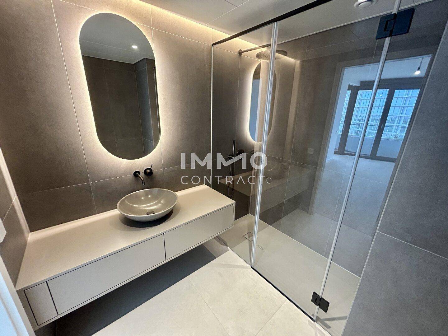 Modernes Badezimmer mit großer Duschkabine, stilvollem Waschbecken und indirekter Beleuchtung.