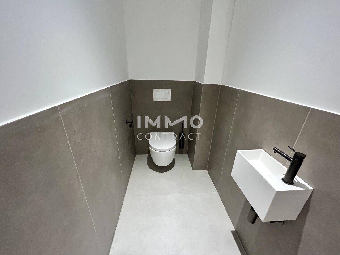 Modernes Gäste-WC mit Wand-WC, kleinem Waschbecken und grauen Fliesen.