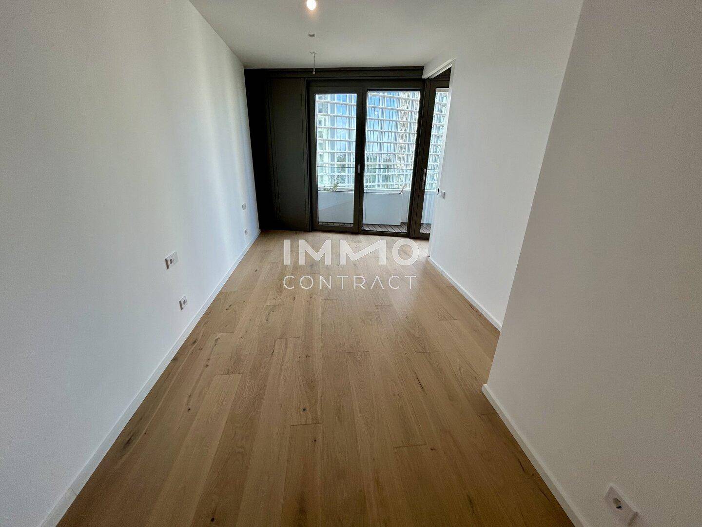 Unmöbliertes Schlafzimmer mit hellem Holzfußboden und Zugang zu einem Balkon.