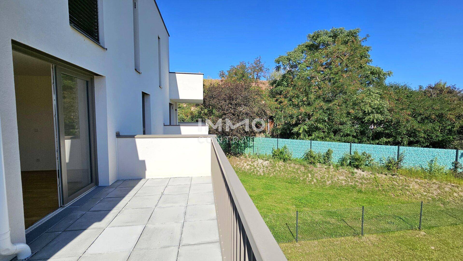 Geräumige Terrasse mit Fliesenboden und Blick auf den Garten sowie die moderne Architektur des Gebäudes.