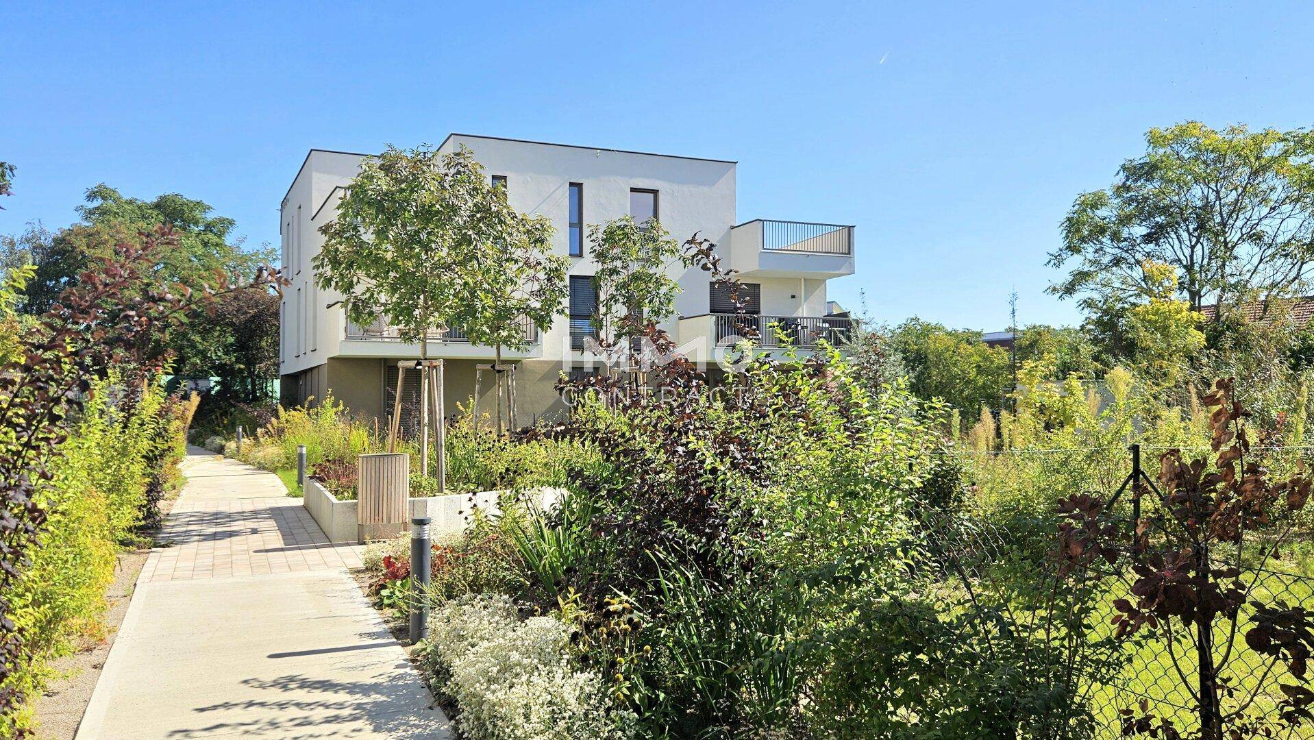 Neubau-Wohngebäude mit zeitgenössischer Architektur, umgeben von gepflegten Grünflächen und Wegen.