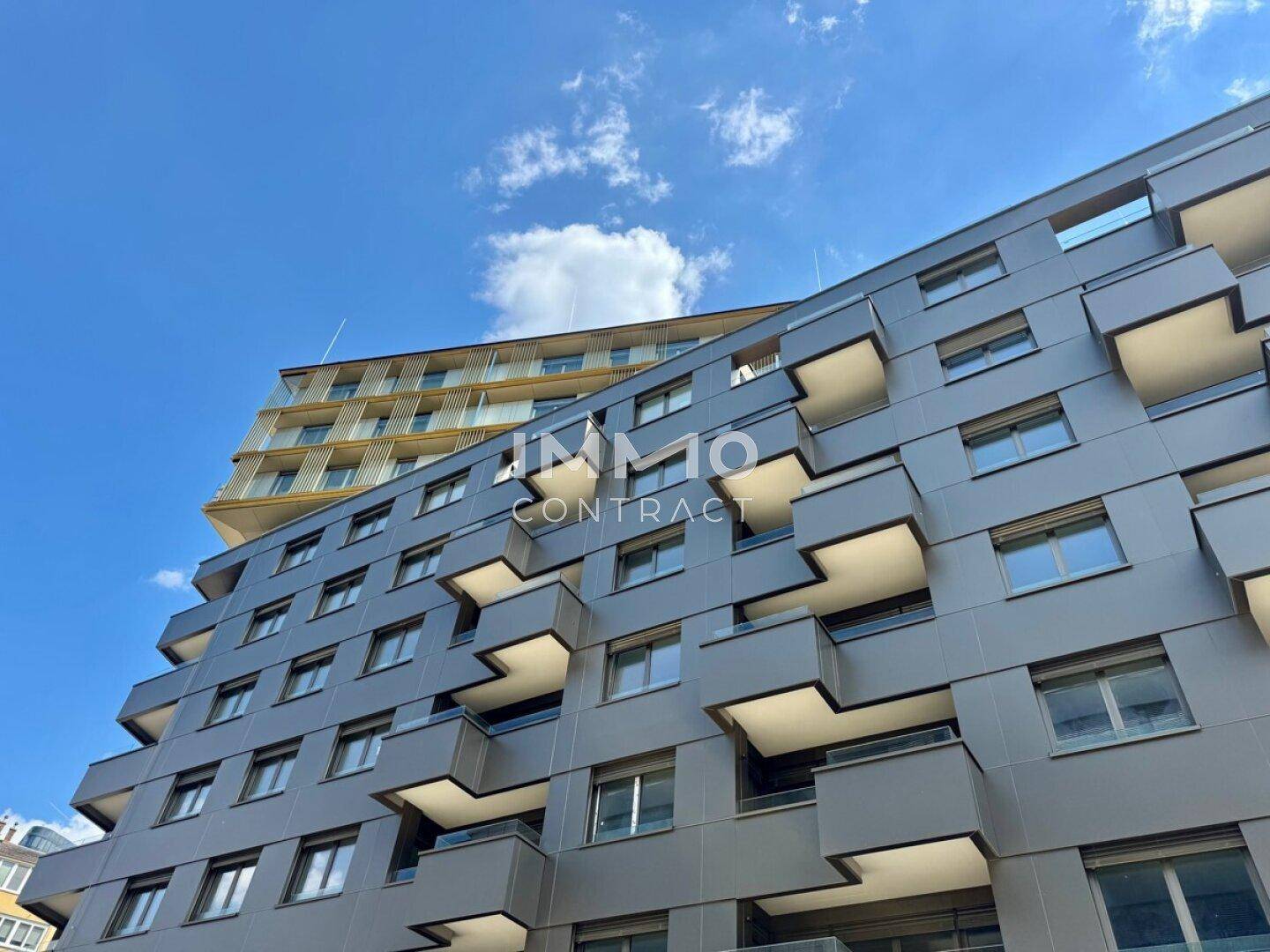 Moderne Gebäudefassade mit gestaffelten Balkonen und großen Fenstern unter blauem Himmel.