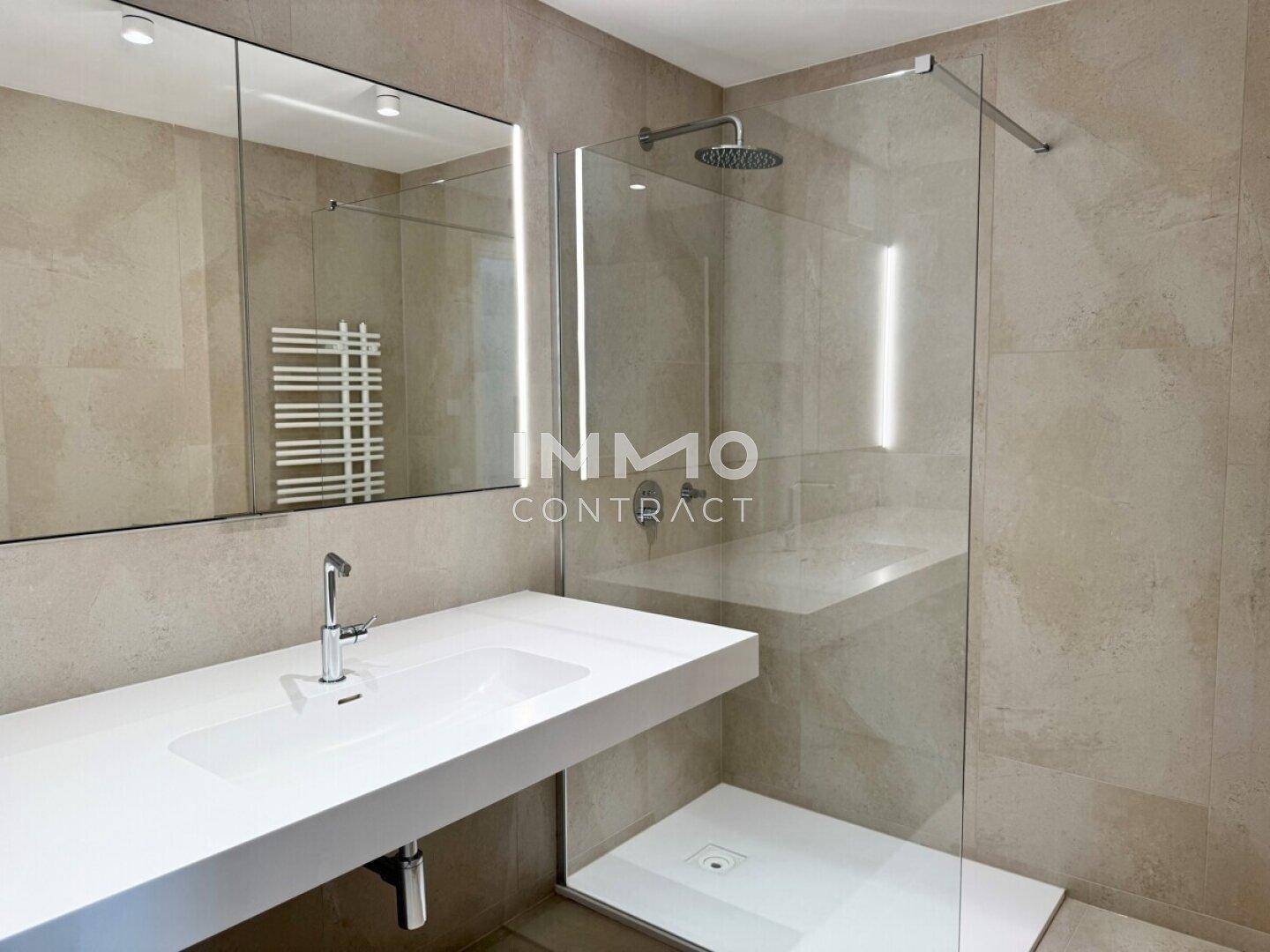 Elegantes Badezimmer mit begehbarer Dusche, modernem Waschbecken und großem Spiegel, alles in hellen Farbtönen.