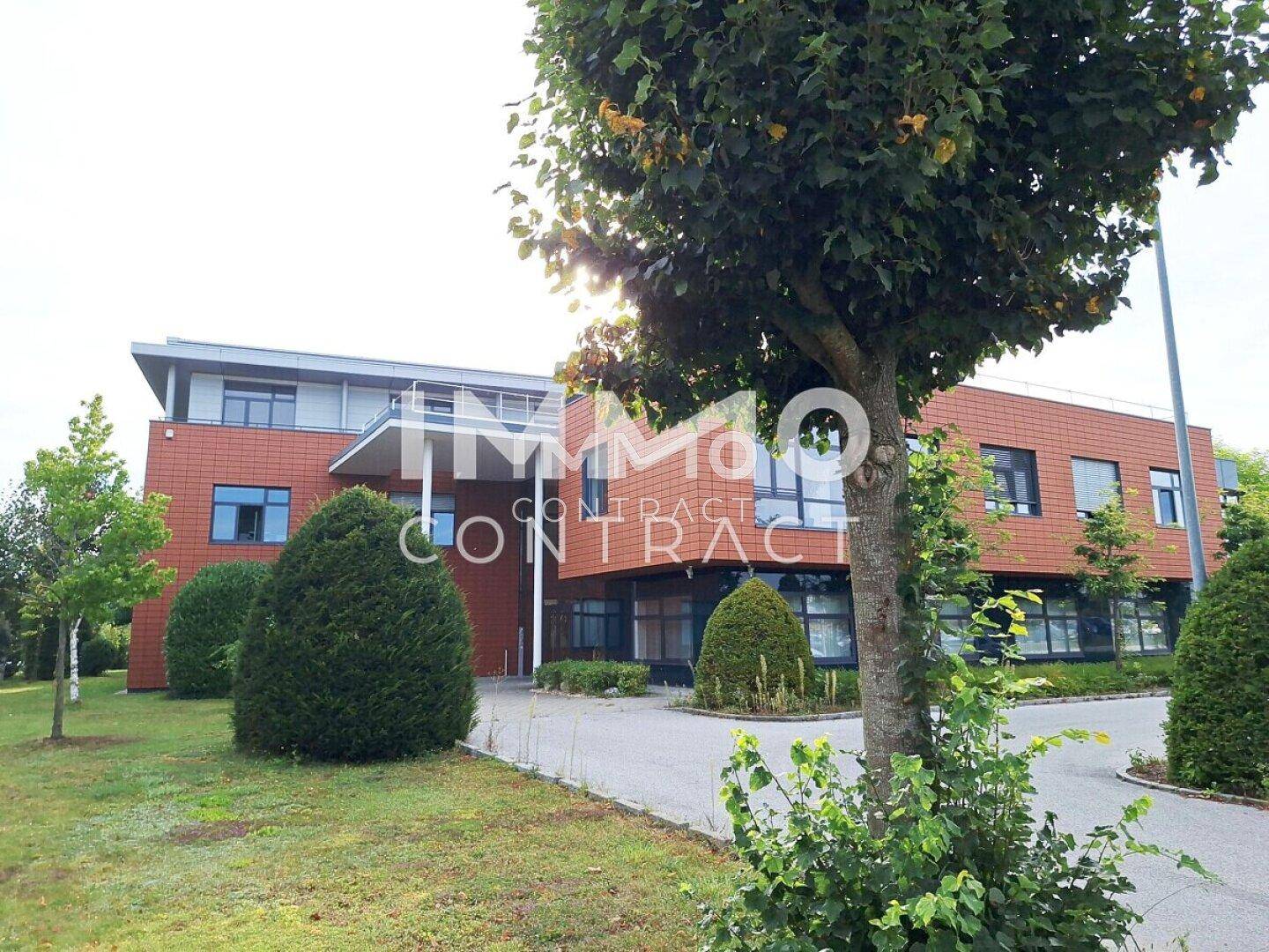 Modernes Bürogebäude mit orangefarbener Fassade und einem gepflegten Vorgartenbereich mit Bäumen und Sträuchern.