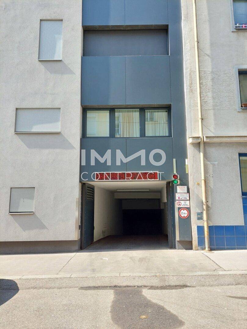 Gebäudefassade mit Einfahrt zu einer Tiefgarage und modernen grauen Elementen.