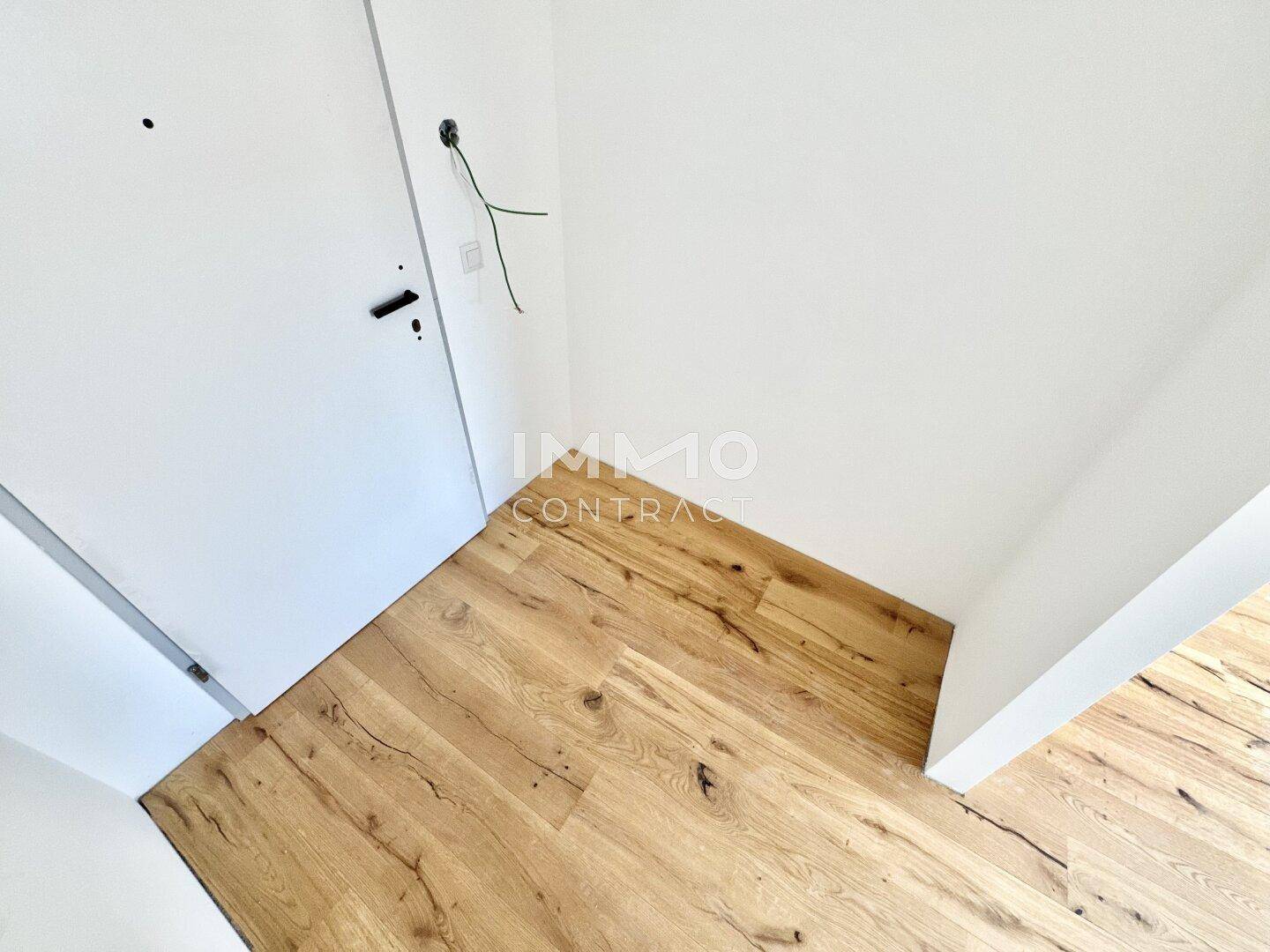Detailansicht eines Türbereichs mit Holzboden und vorbereiteten Elektroinstallationen.