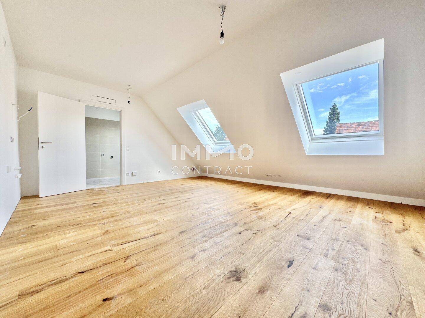 Leerer Dachraum mit Holzboden, schrägen Decken und großen Dachfenstern, bereit zur Einrichtung.