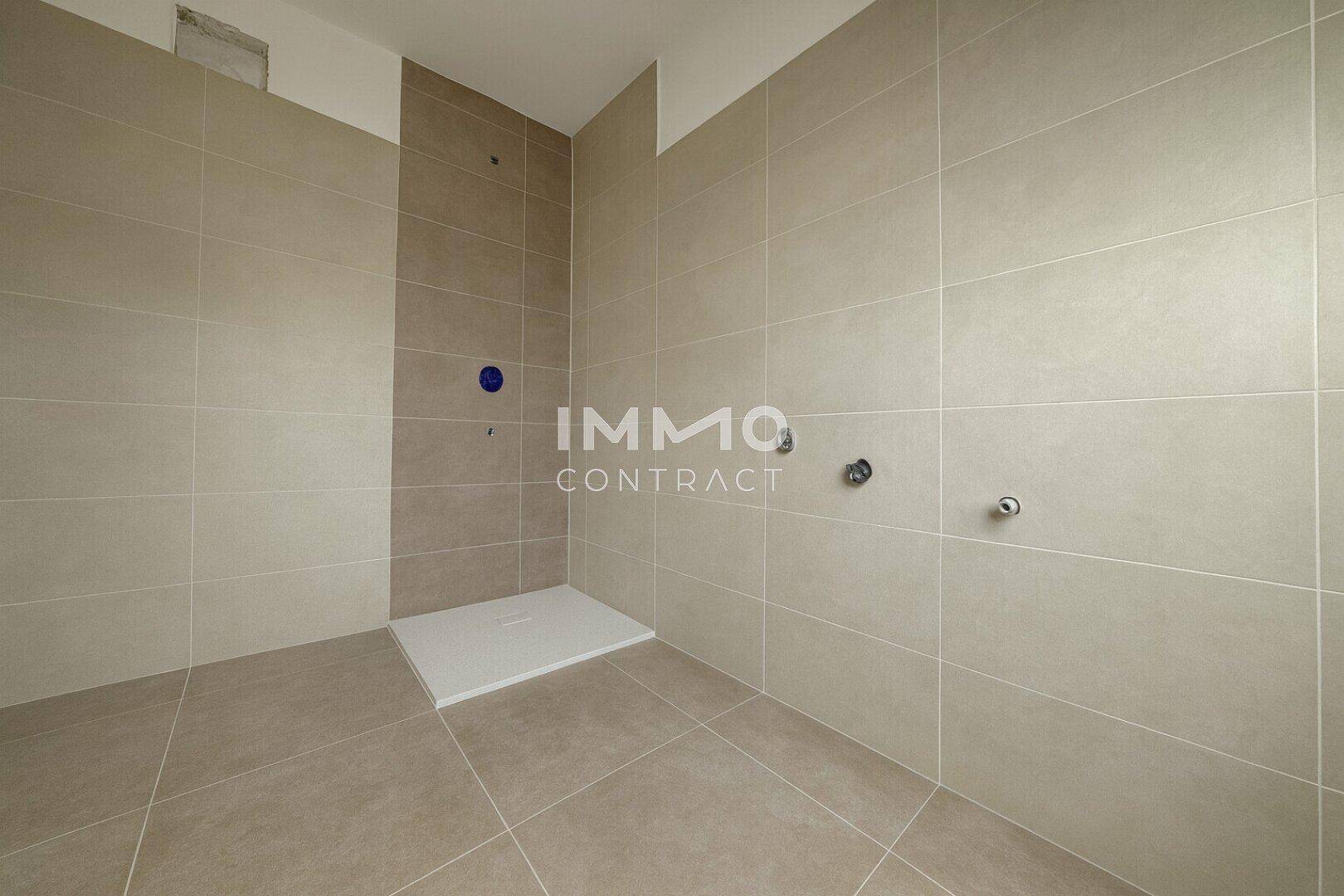 Modernes Badezimmer mit beigefarbenen Fliesen und vorbereiteter Duschwanne, noch ohne Armaturen.
