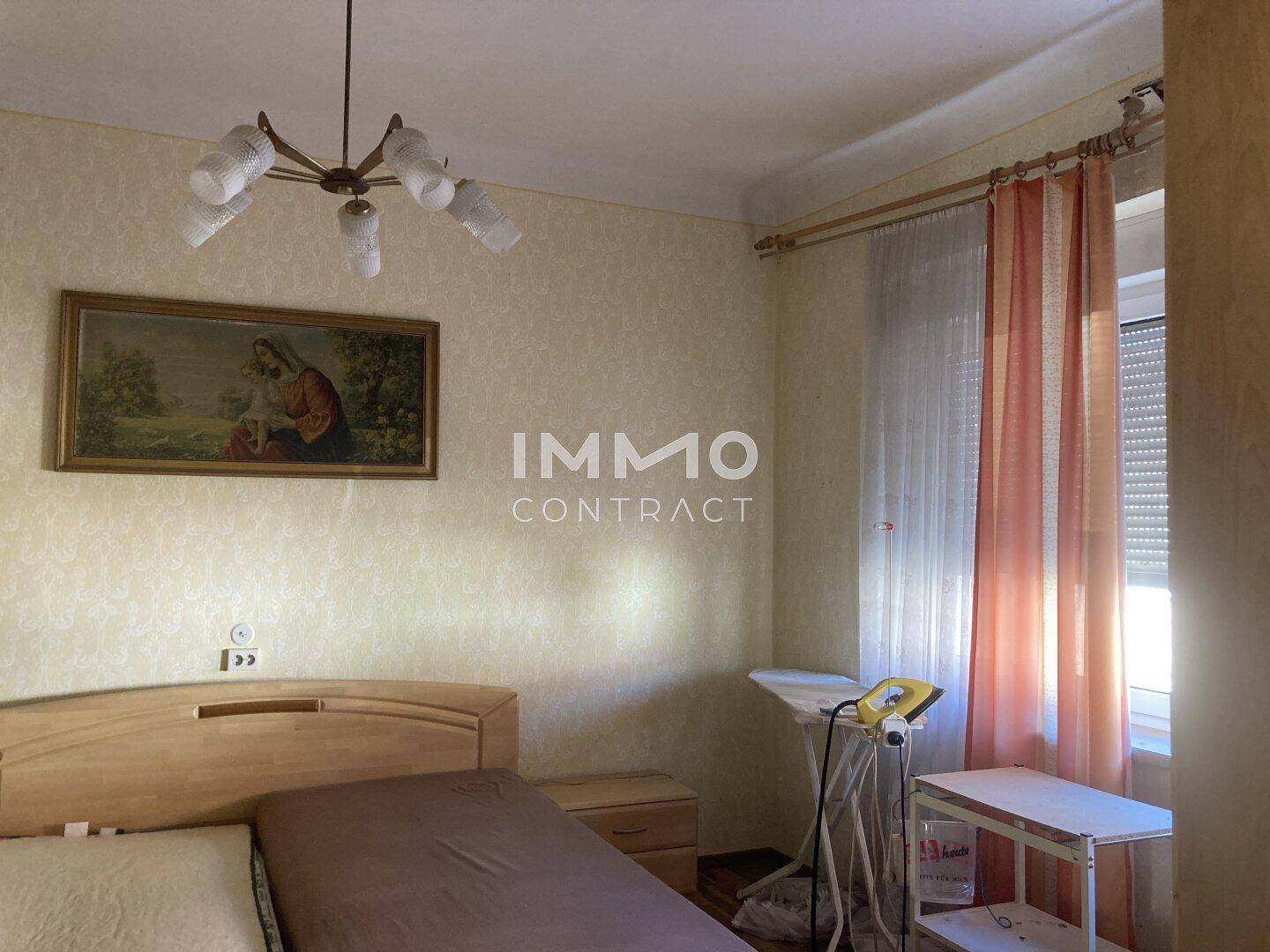 Schlafzimmer mit Bett, traditioneller Tapete und einem Fenster mit Jalousien.