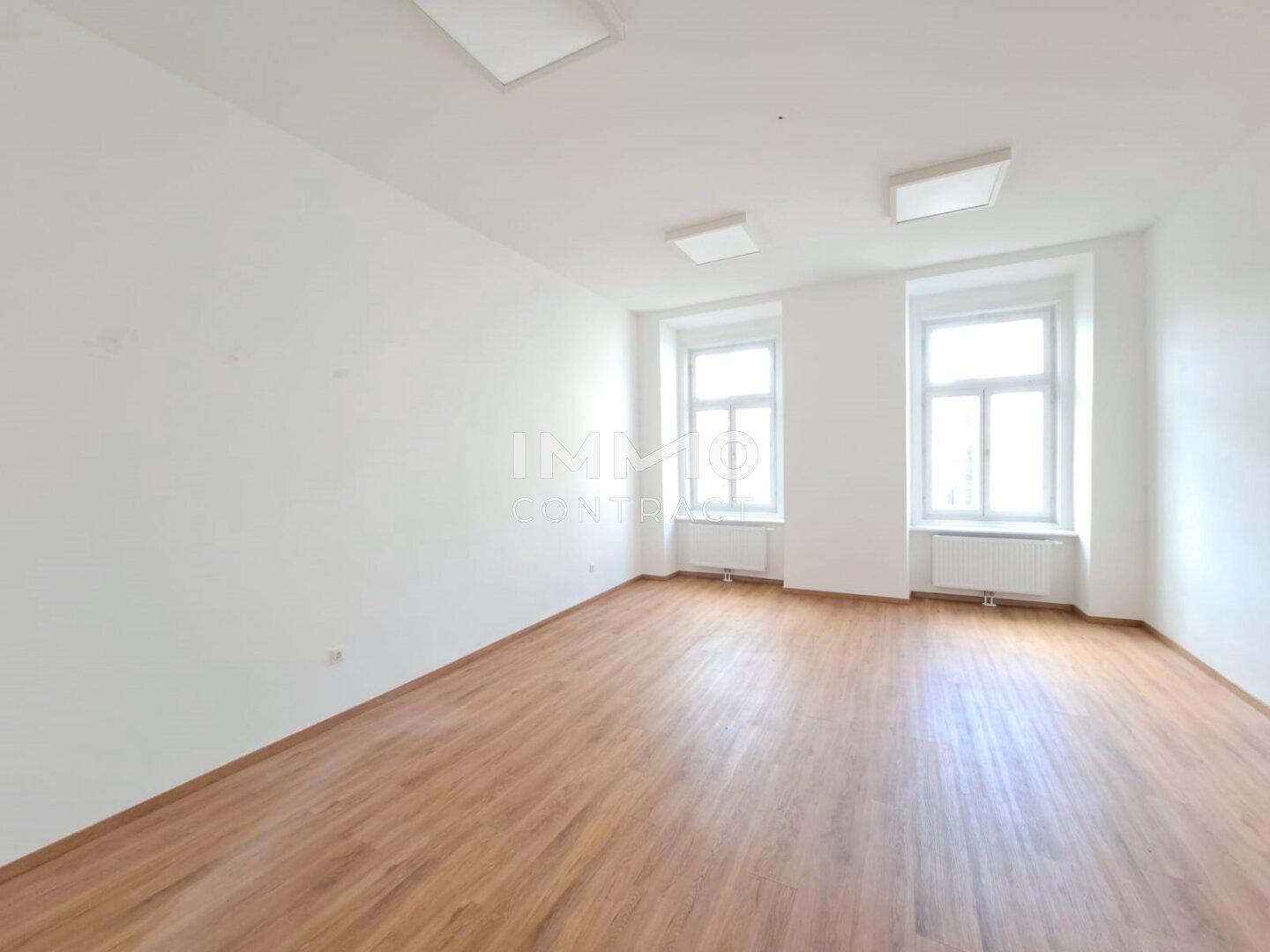 Heller, leerer Raum mit zwei Fenstern und Holzboden, ideal für verschiedene Nutzungsmöglichkeiten.