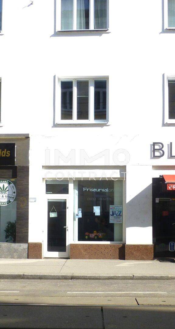 Nahaufnahme eines Friseursalons im Erdgeschoss eines weißen Gebäudes mit großen Schaufenstern.